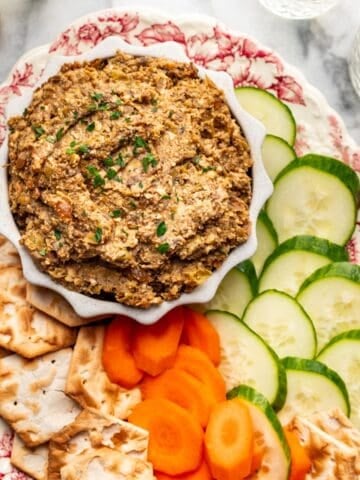 Vegetarian chopped liver in a serving bowl with cucumbers, carrots, and crackers on the side.