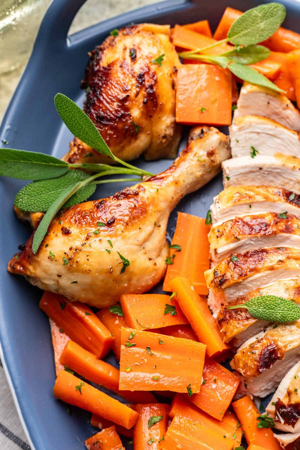 Roasted chicken leg and sliced chicken breast on a serving platter with cooked carrots.