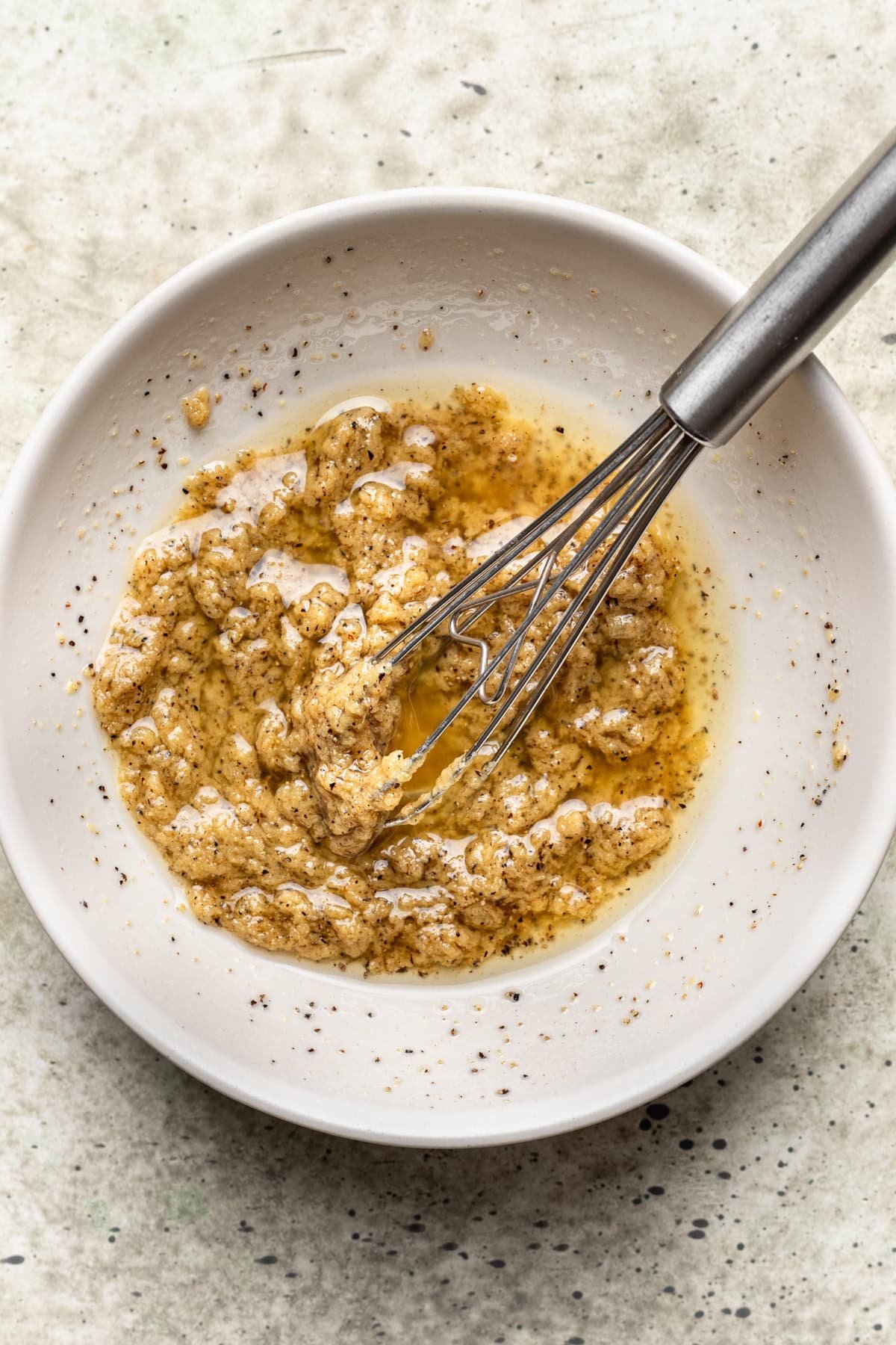 Oil, seasoning, and mustard mixture whisked in a bowl.
