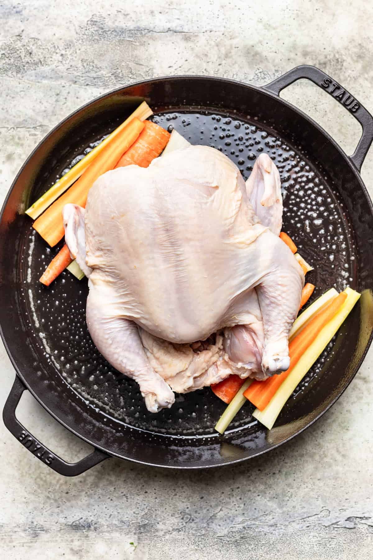 Carrots, celery, and raw whole chicken in a roasting pan.