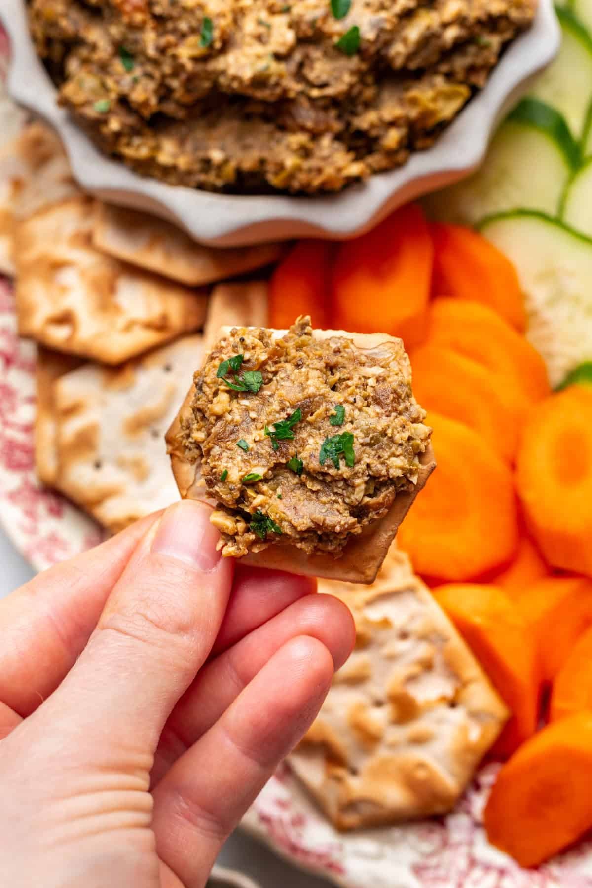 A hand holding vegetarian chopped liver scooped on a cracker.