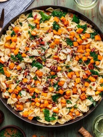 Roasted butternut squash pasta with ground chicken and kale in a large black skillet.
