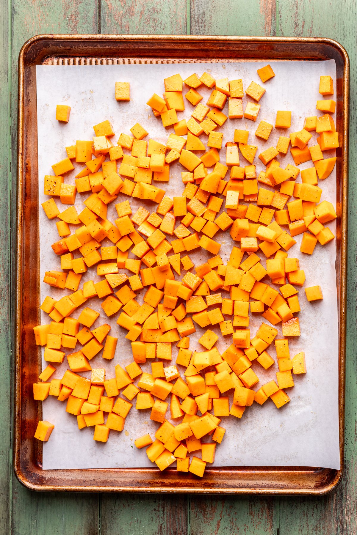 Raw cubes of butternut squash on a large baking sheet.