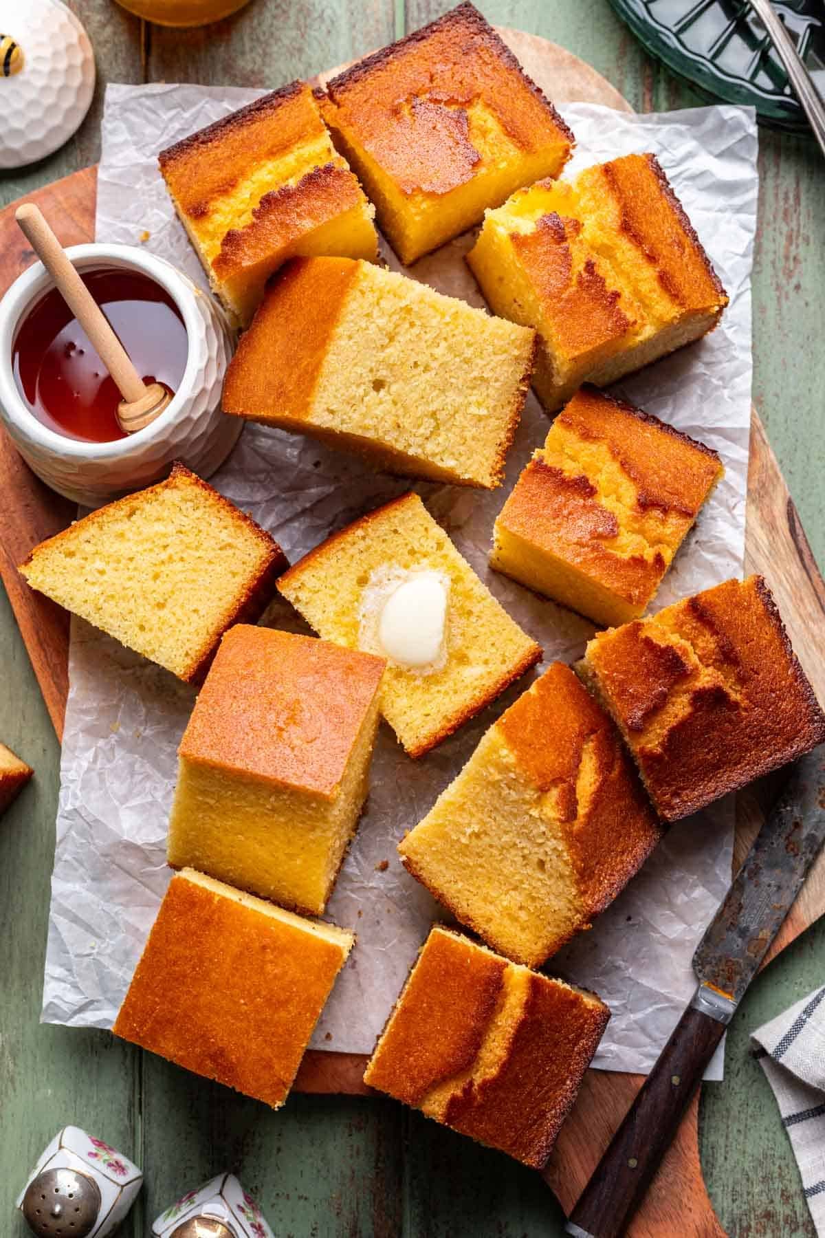 Slices of cornbread on a wood serving board with honey on the side.