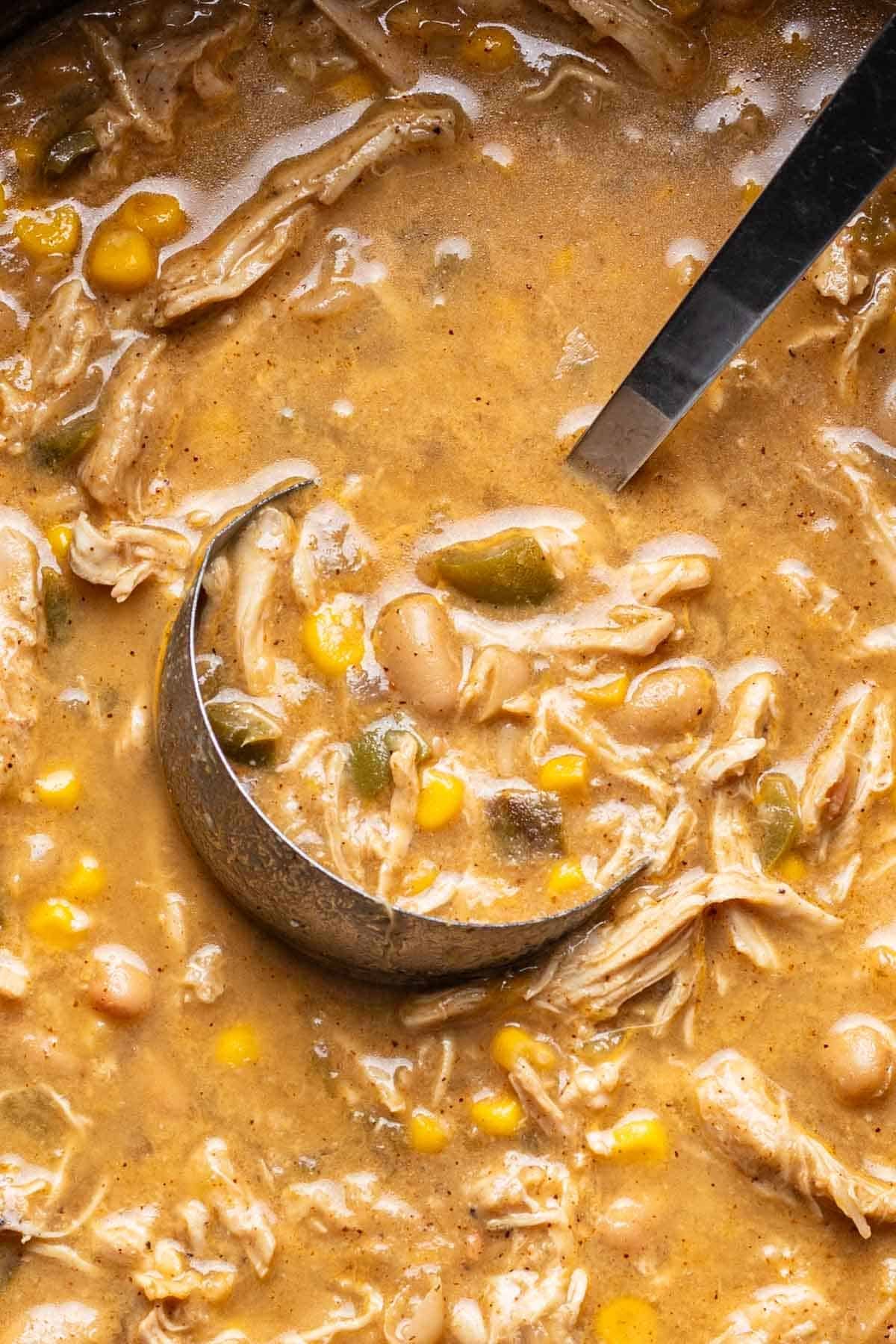 A ladle scooping white chicken chili out of a pot.